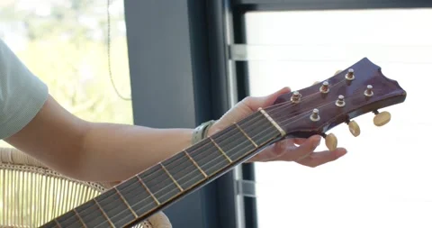 Left hand is touching tuning pegs and tightening strings to tune acoustic guitar Stock Footage 339321014