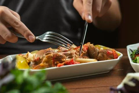Left-handed man eats lamb stew on the bone with vegetables. Khashlama is popu Stock-Fotos