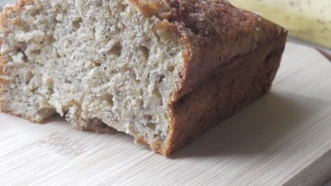 Left pan of banana bread cut in half on a wooden board with a banana in the 스톡 동영상 296574874