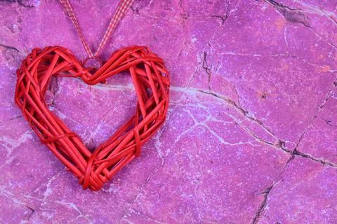 On the left side of the pink marble background lies a decorative heart in red Stock Photos