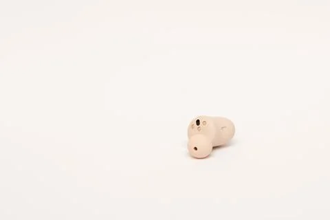 Left wireless earbud earbud close-up on light background. Stock Photos