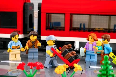 Lego porter with stack of suitcases and some passengers on the platform in fr Stock Photos