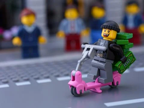 Lego robber riding scooter with stack of money in front of a crowd of people Stock Photos