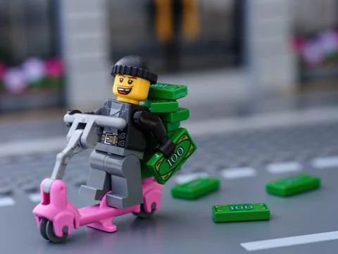 Lego robber riding a scooter with stack of money and dropping money on street Stock Photos