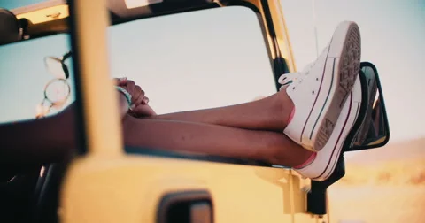 Legs and feet sticking out of car window on road trip Stock Footage