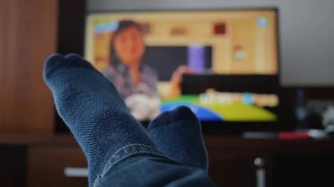 Legs in blue socks lie in front of the TV. Close-up on his feet. Cozy atmosphere Vidéo 115335843