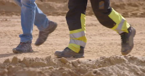 Legs of a builder in overalls and his boss walk along a dirt road Stock Footage 161957674