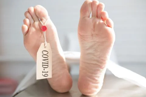 Legs of a corpse in a morgue on a table with a tag with the inscription COVID Stock-Fotos