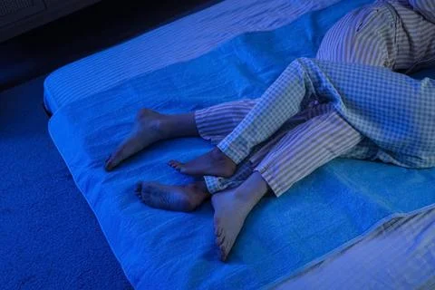 Legs of couple sleeping on electric heating pad in bedroom at night Fotos Stock