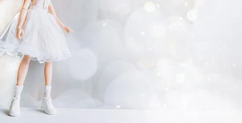 Legs of a doll in a white dress and shoes on a white background in the format of Stock Photos