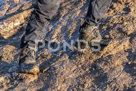 Legs in gray pants and trek boots hiking upwards on muddy hill at evening Stock Photos
