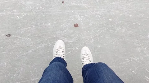 Legs in jeans and skates dangle over the ice rink. Winter ice rink in the park. Video stock 233517652