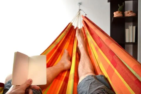 Legs of man lying down in bright hammock holding empty notice book in his han Stock Photos