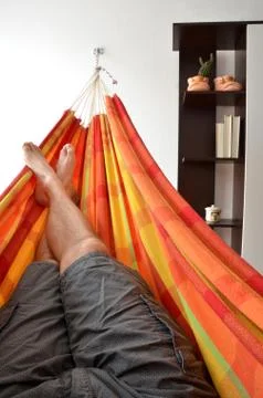 Legs of man lying down in bright hammock attached on house wall next to book- Stock Photos