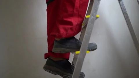 Legs of an unrecognizable worker in red overalls climbing a stepladder Stock Footage 163833249