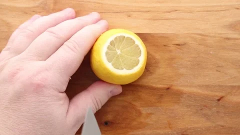 A lemon being squeezed by hand over a wooden surface, extracting fresh juice. Stock Footage 311046419