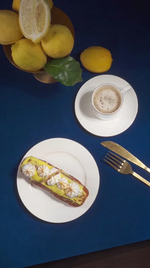 Lemon Eclair Dessert and Coffee Serving on Cafe Table with Fork and Spoon Close Stock Footage 335422295