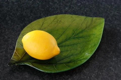 Lemon on a green leaf-shaped plate, on a dark granite background Stock Photos
