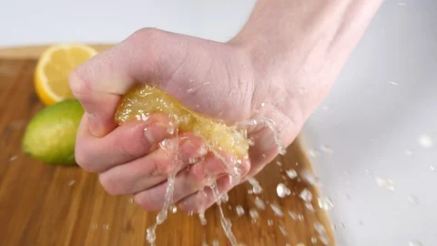 A lemon in half with mans hand squeezing to juice dripping onto a wooden board Stock Footage 88512420