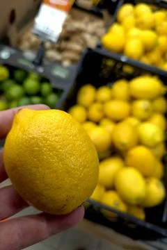 Lemon Held by Hand With Stacks of Lemons in Background at Grocery Store Stock Photos