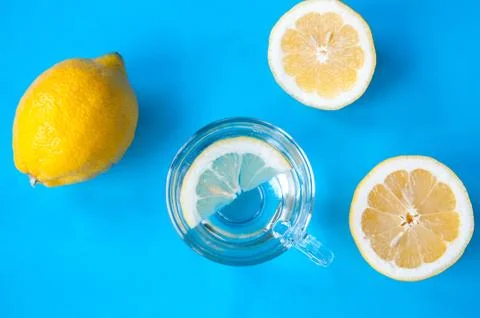 Lemon parts and transparent mug with lemon on a blue background, cold and flu Stock Photos