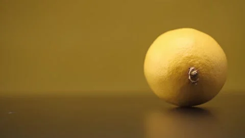 A lemon rolls on a black table on a yellow background. Close up. Stock Footage 144334342