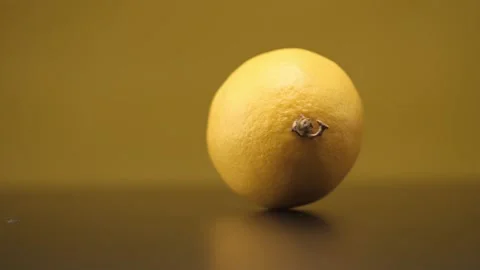 A lemon rolls on a black table on a yellow background. Close up. Stock Footage 144334343
