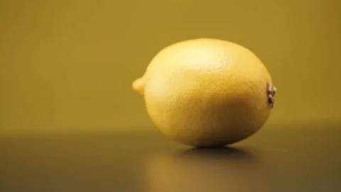 A lemon rolls on a black table on a yellow background. Close up. Stock Footage 144334369