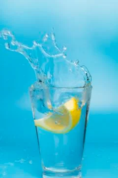 Lemon slice falling and dropping into a splashing glass with light blue backg Stock Photos
