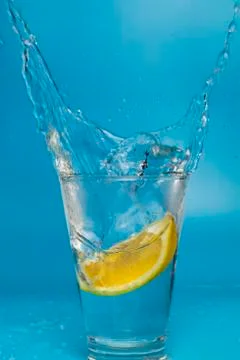 Lemon slice falling and dropping into a splashing glass with light blue backg Stock Photos