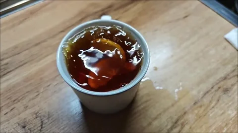 Lemon slice falling and splashing in a white teacup full of tea, on a wooden Vidéo 307494168