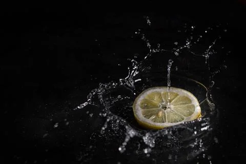Lemon slice falling into the water with black background. Stock Photos