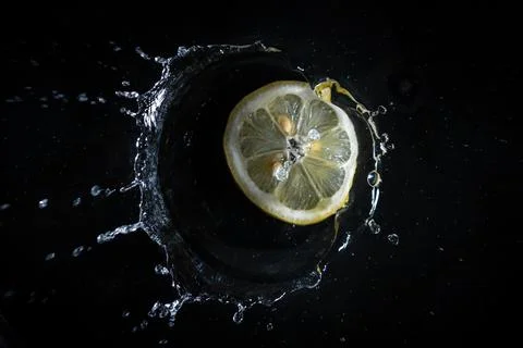 Lemon slice falling into the water with black background. Stock Photos
