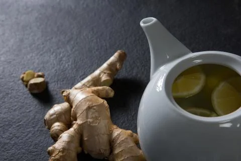 Lemon slice in teapot with ginger on black background Stock Photos