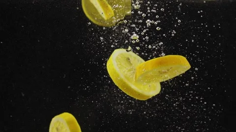 Lemon slices dropping or falling in clear water with bubbles over back Stock Footage 293086224