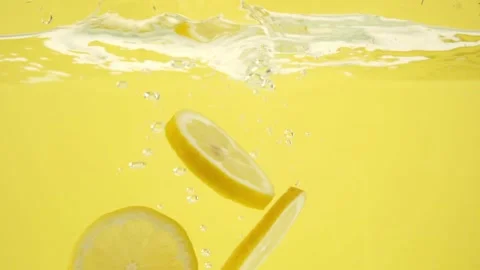 Lemon slices falling into a water with splashes isolated on yellow background 库存影片 153479592