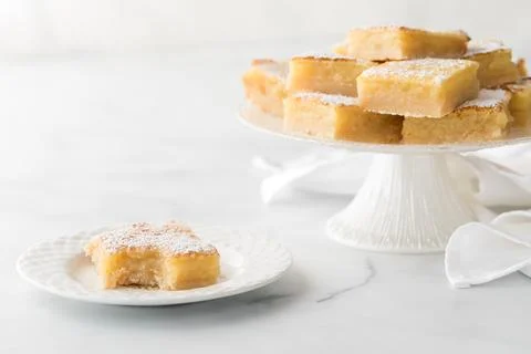 A lemon square with a bite out in front of a stand full of lemon squares. Stock Photos