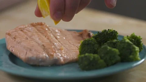 A lemon is squeezed onto a plated piece of salmon. Stock Footage 72544430
