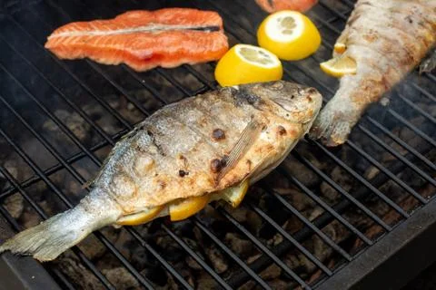 Lemon stuffed fish lying on the grill grate. Stock Photos