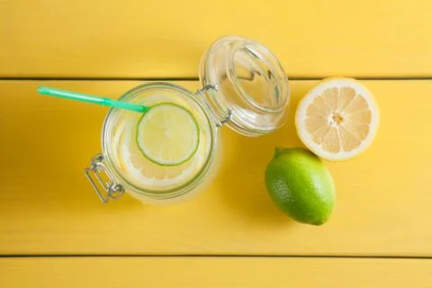 Lemonade with ice, lemon and lime in a jar on a yellow wooden background. Stock Photos