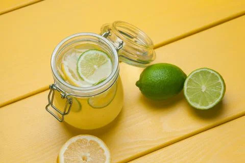Lemonade with ice, lemon and lime in a jar on a yellow wooden background. Stock Photos