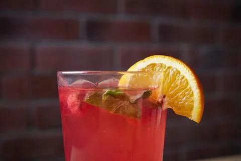 Lemonade on table, mint and lemon wedge, glass with straw, brick wall on Stock Photos