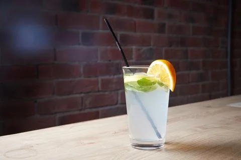 Lemonade on table, mint and lemon wedge, glass with straw, brick wall on Stock Photos