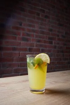 Lemonade on table, mint and lemon wedge, glass with straw, brick wall on Stock Photos