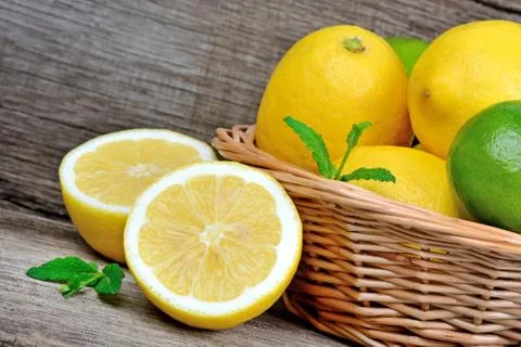 Lemons and limes with mint in a basket on table Stock Photos
