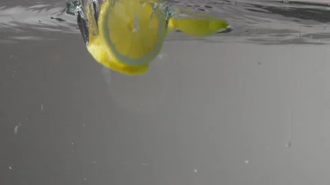 Lemons cut and droped into the transparent aquarium with water on grey Stock Footage 133228344