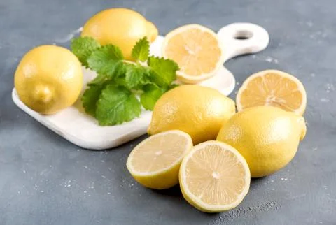 Lemons on cutting board on grey background Fresh yellow citrus Mint leaf Stock Photos