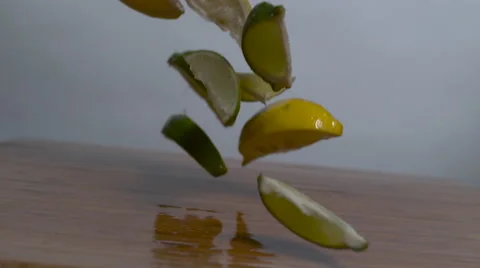 Lemons &amp; Limes wedges falling in slow motion onto a cutting board Stock Footage 64699776