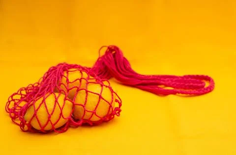Lemons in red eco shopping string bag on yellow background. Eco friendly conc Stock Photos
