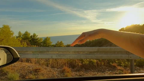 LENS FLARE: Hand makes waves through car window while driving along the seashore Stock Footage 241308638